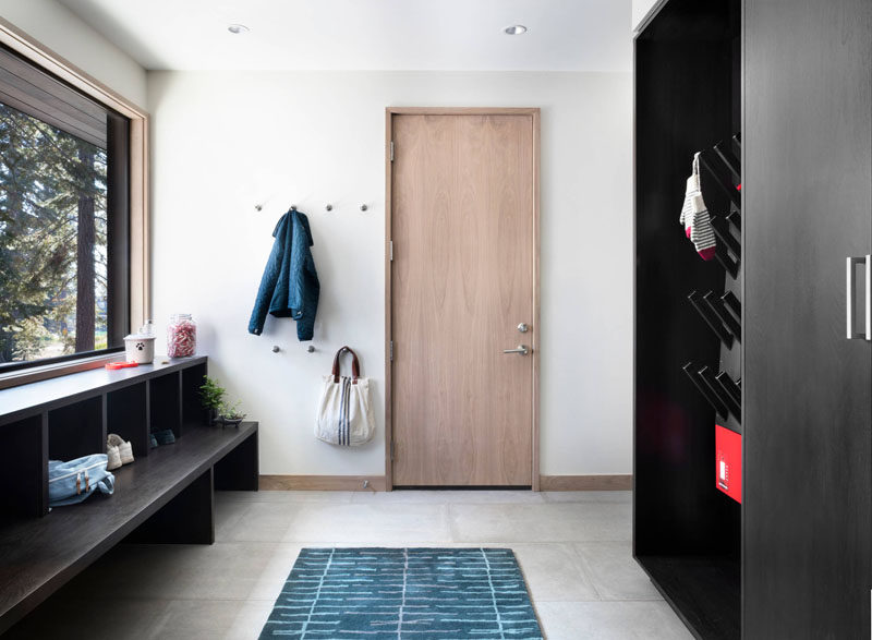 The large window in this modern mudroom lets in plenty of light that's reflected off the white walls. Tiny wall hooks create an area to hang your jacket, while a dark wood drying rack sits on one wall, and under the window a bench with open storage cubbies creates a spot for putting on your shoes.