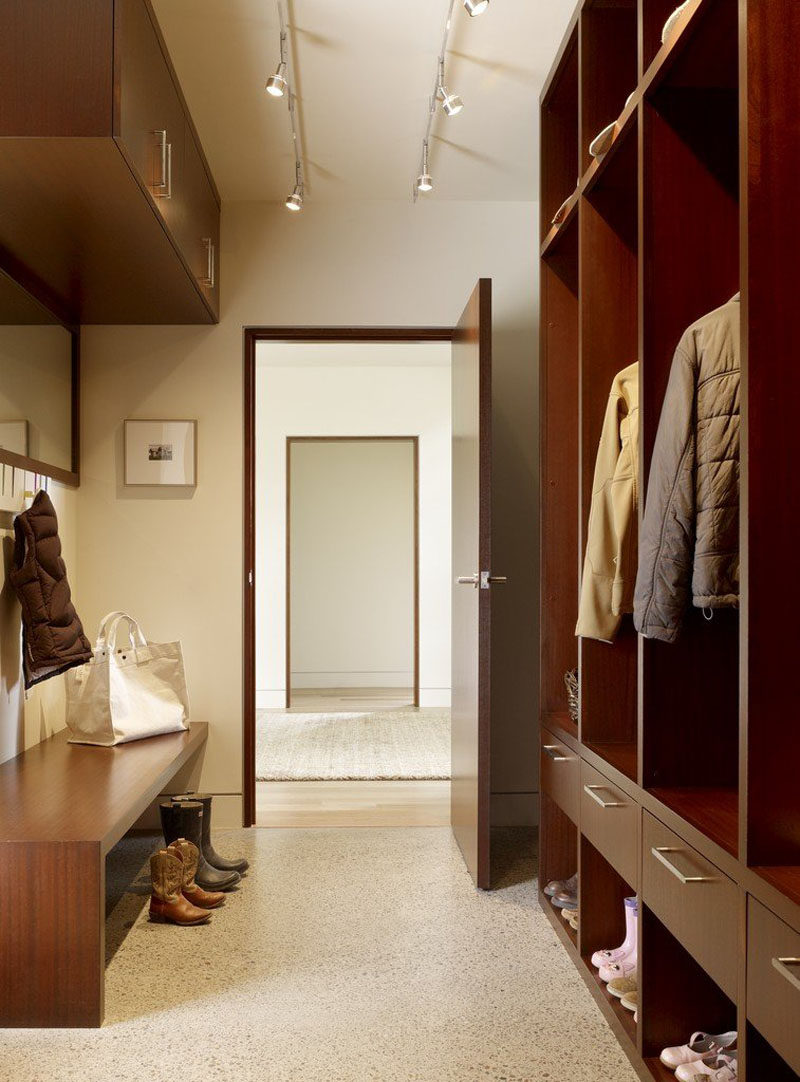 Open storage closets made with drawers and shoe cubbies keep the family organized in this small modern mudroom. On the opposite wall is a built-in wood bench, and hanging above it is a mirror with small hooks and additional wall-mounted storage cabinets.