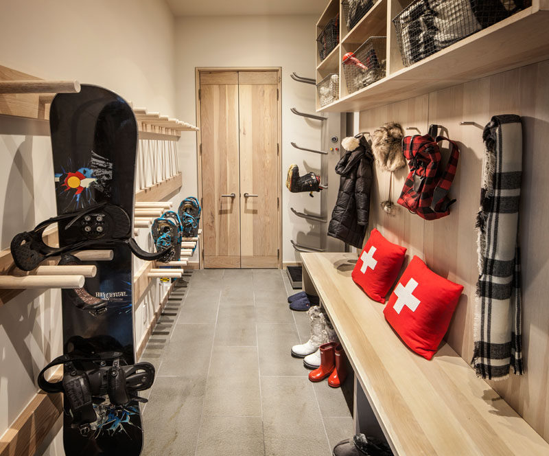 This mudroom (or winter sport storage space) is perfectly designed with light wood cabinets, racks and hooks. A wood bench makes it easy to take off boots, and upper storage spaces with wire baskets keep things organized.