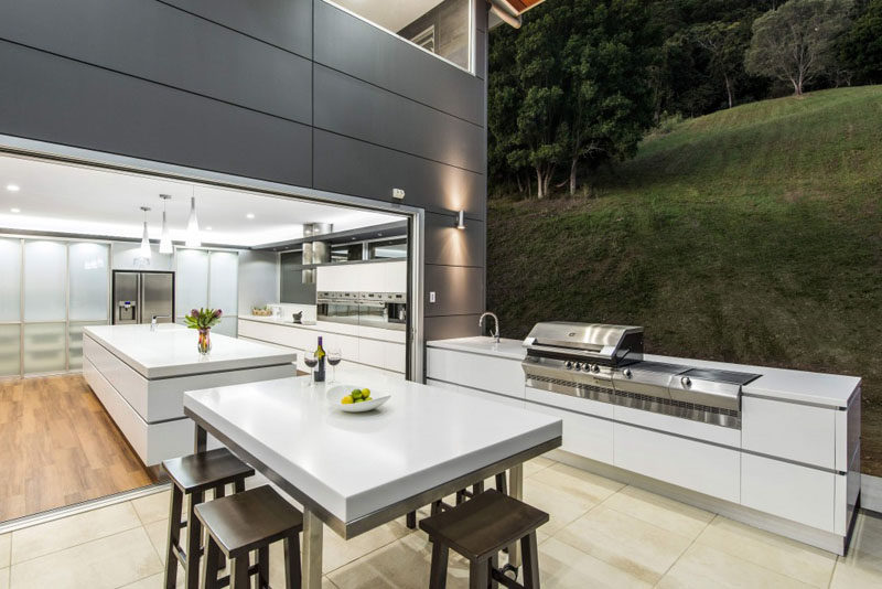 This modern outdoor kitchen appears as an extension of the interior kitchen with the same white cabinets and stainless steel appliances.