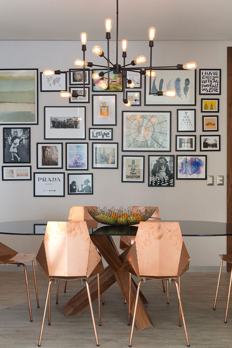 Prints and photos surrounded by simple black frames hang on the wall behind the dining table in this apartment and add color, personality, and life to the interior.