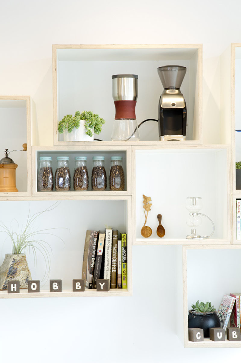 In this modern coffee shop design, there's a floating wood shelf made from rectangular boxes to display various items.