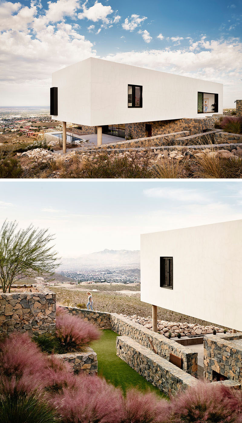 This modern house has a landscaped yard with stone walls. The house features black window frames that contrast the white exterior walls.