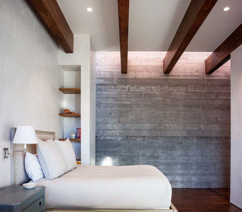 In this modern guest bedroom, the concrete and white walls are broken up by the use of dark wood beams, shelves and flooring.