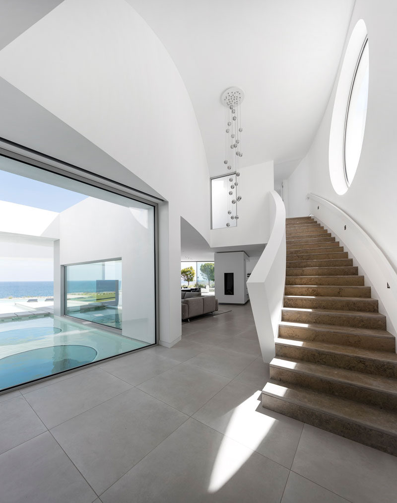 Inside this modern house with a white interior is a curved staircase with a large circular window that leads you to the upper level of the home.