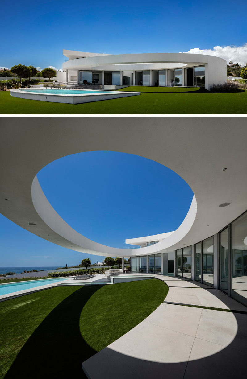 This modern sculptural house has a large landscaped backyard that's home to a swimming pool and tiered outdoor patio area, set up for lounging. A large ellipse cut out in the house design adds a sculptural touch.