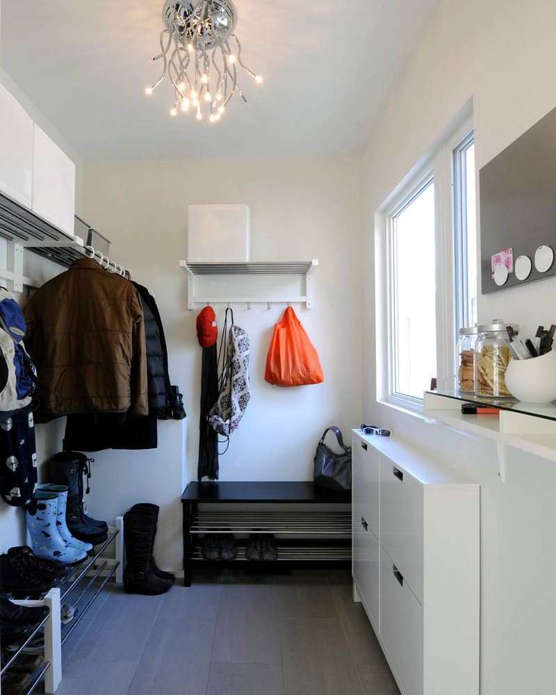 In this mostly white modern mudroom, there's plenty of shoe storage in the form of shoe racks, while above them are spaces to hang coats. Thin wall mounted cabinets under the window give each family member a place to store bits and pieces, and white cubes and metal bins on top of the hanging racks create extra storage space. A little shelf is home to containers of snacks and pens, and a magnet boards lets family members leave notes for each other.