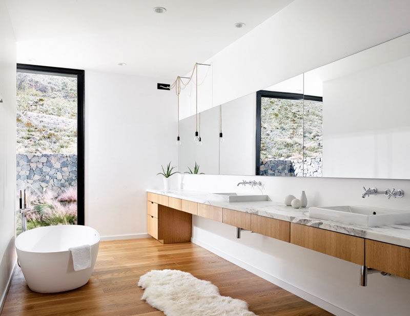 In this modern master bathroom, white walls, a white oak vanity and matching floors, a white stand alone tub, and marble countertop give the bathroom a sophisticated and luxurious feel that's bright and airy.