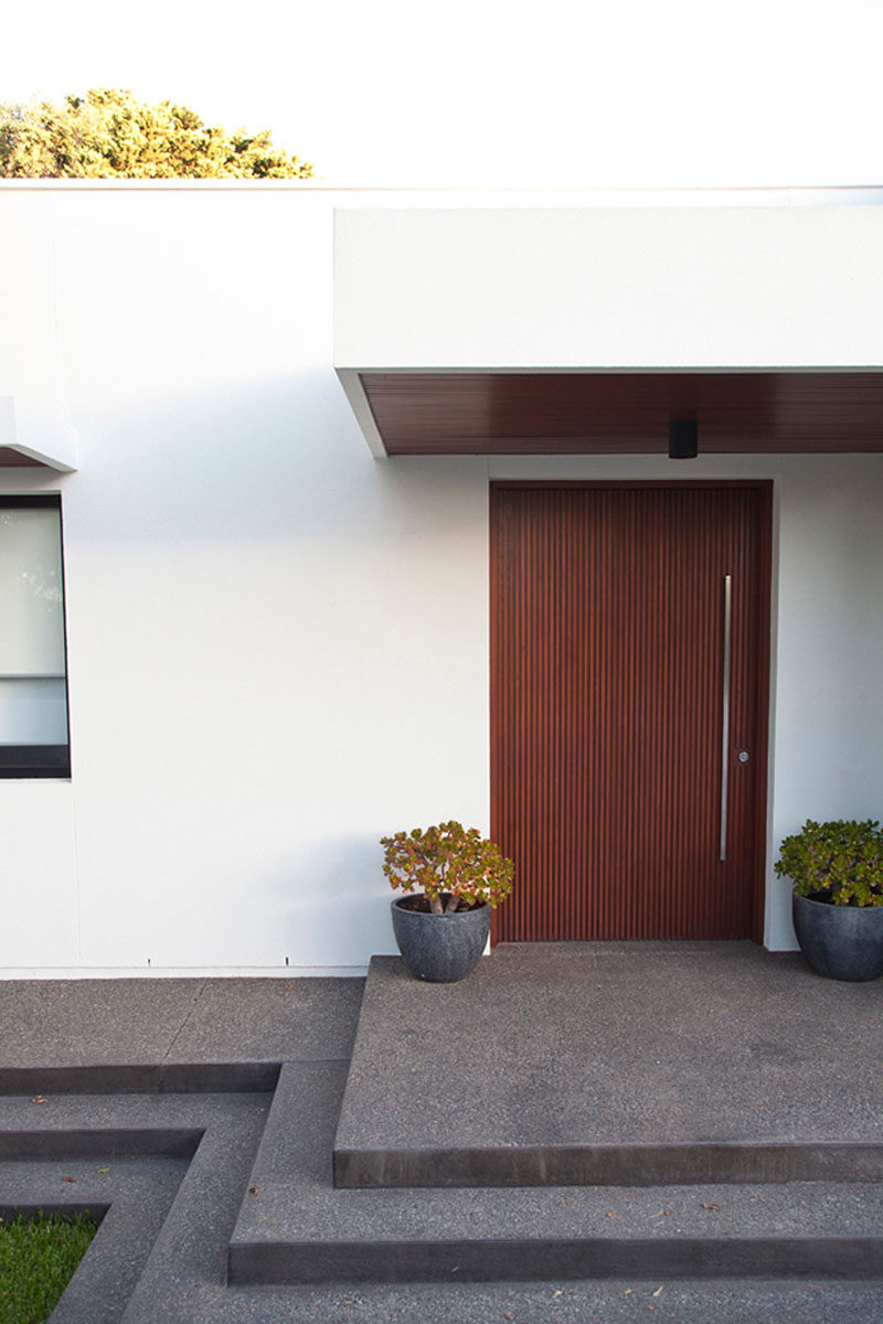 The dark wood door leading into this Australian home has vertical lines and a tall, thin, vertically placed minimalist metal door handle follows the lines in the wood.