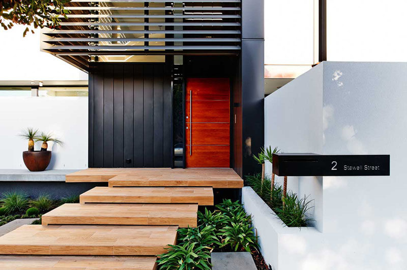 This large wood door, made up of four rich wood panels and a silver metal door handle, warms up the black metal panels and creates a contemporary look on the exterior of this Australian home.