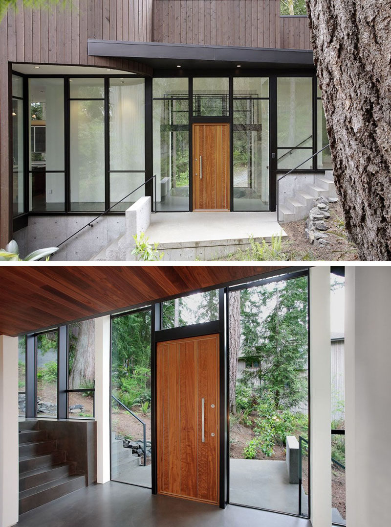 This light wood paneled door, featuring a silver door handle, is surrounded by a wall of windows and black steel frames that create a modern entryway full of natural light.
