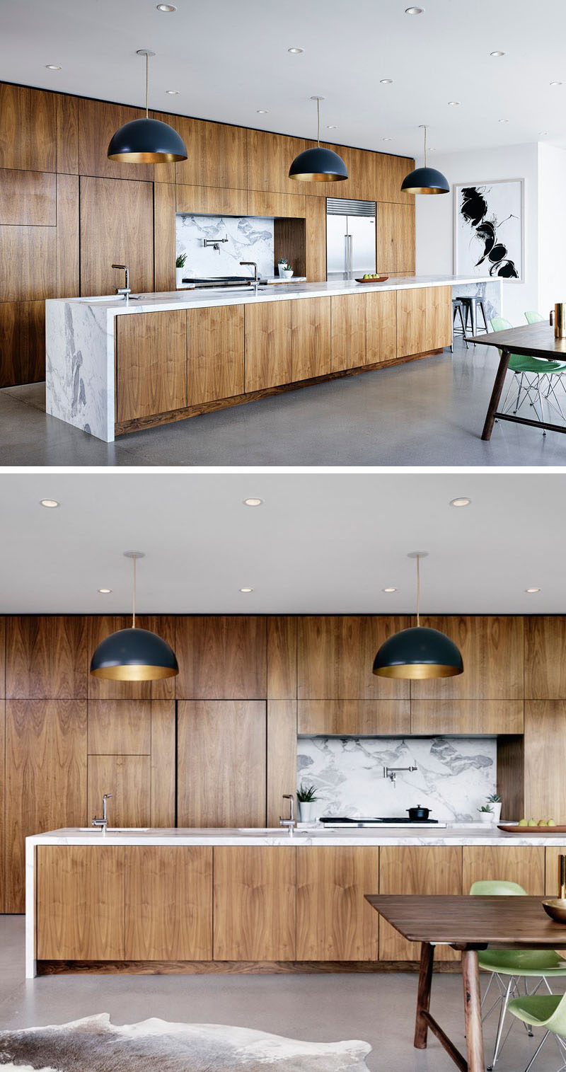 Polished concrete floors and white walls and ceiling give the kitchen a modern, clean feel that's warmed up by the American black walnut covering the cabinets on the wall and on the island. The marble countertops and backsplash add a luxurious touch to the warm wood and pendant lighting above the island helps brighten the space once the sun goes down.