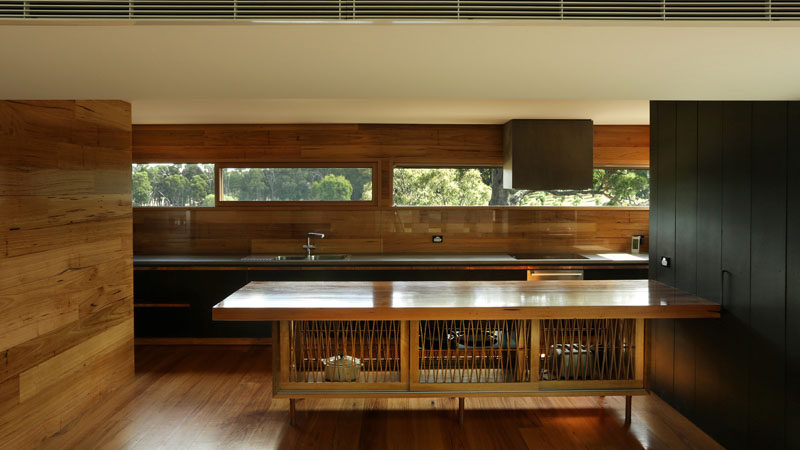 In this wood-clad kitchen, the large island features artistic doors and black wood cabinets add a modern touch to the room, while a letterbox window along the back wall connects the kitchen to the outdoors.