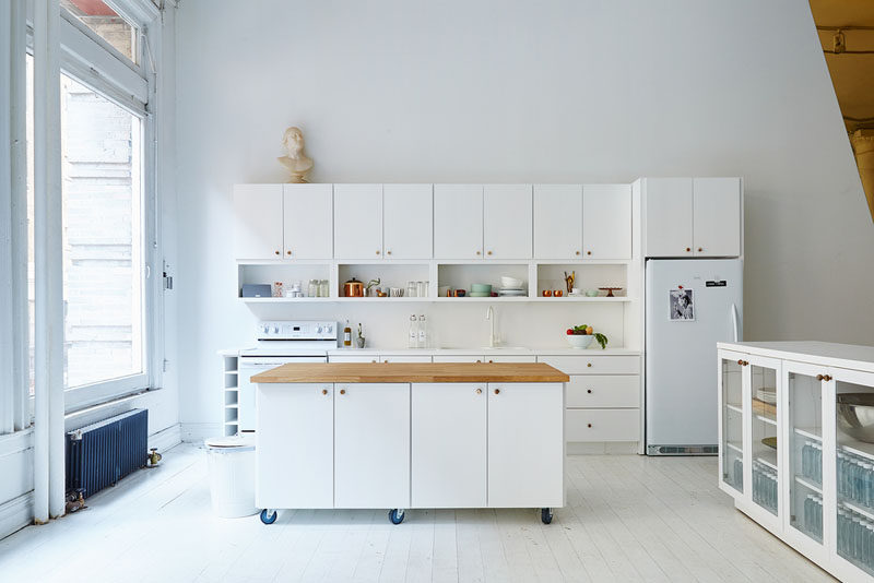 The wheels on the bottom of this movable white kitchen island with a wood countertop, lets people move it around so they can prep things closer to the rest of the counter or move it out of the way entirely when they need more floor space.