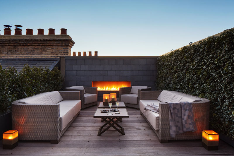 This rooftop combines a built-in fireplace, plant-covered walls, wood flooring, and comfortable outdoor furniture, to create a quiet escape from busy London life.