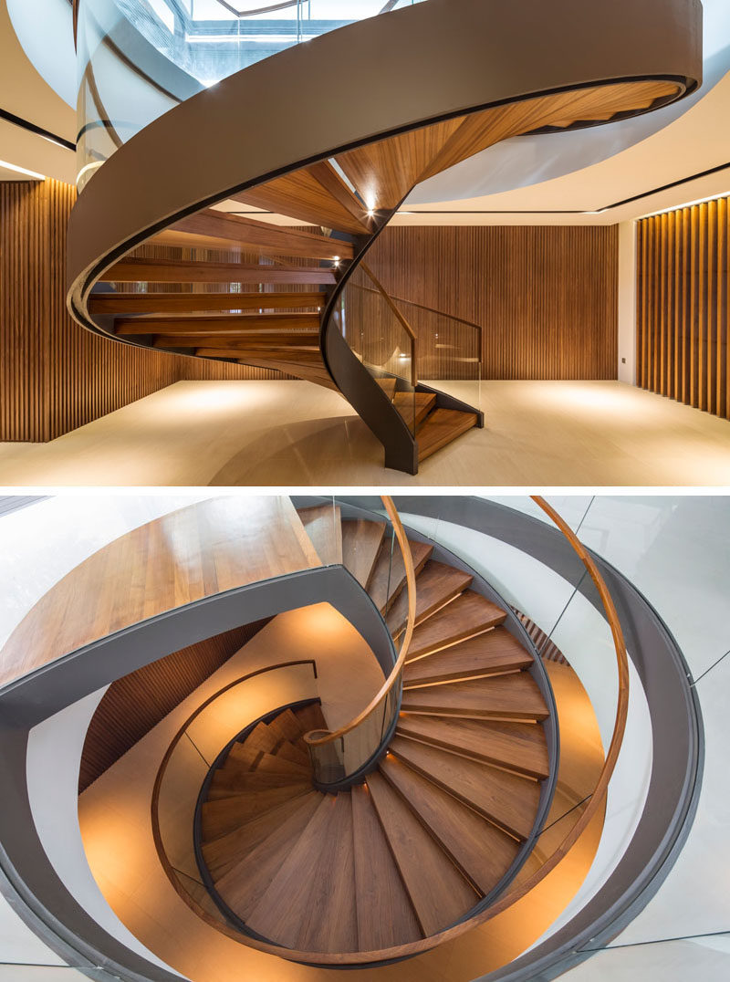 This large sculptural spiral staircase that rises up from the basement to the main floor of the home has wood treads and glass safety railings that let light pass through them to keep the spaces feeling bright. #SpiralStairs #SpiralStaircase #ModernSpiralStairs