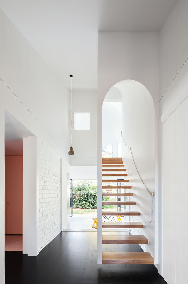 A white arched wooden staircase leads up to the second story of the extension of this renovated house.