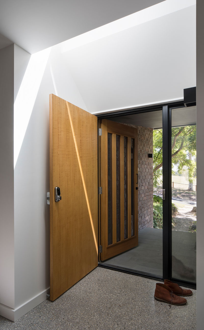 In the entryway of this modern house, a skylight is positioned directly above the wooden front door lets natural light to fill the space.