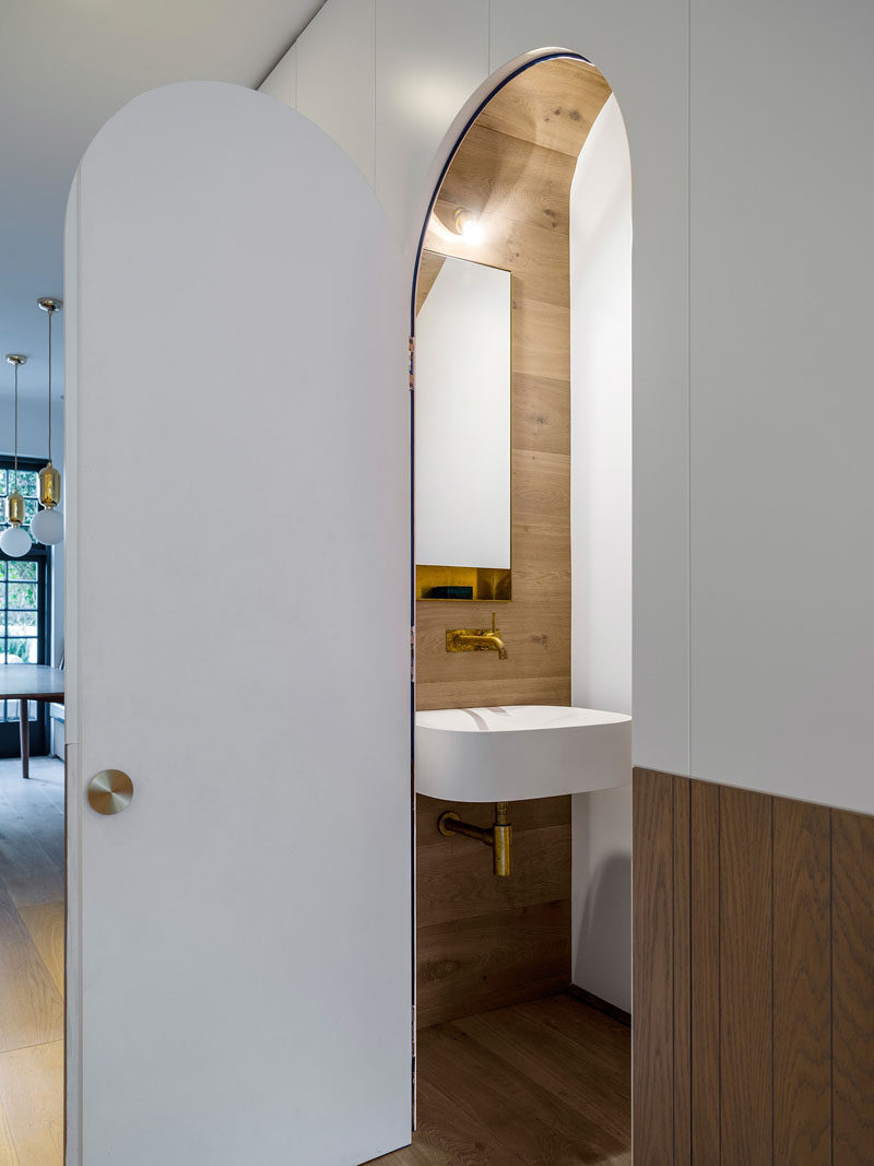 In this modern house, there's a hidden powder room with an arched door located under the stairs.