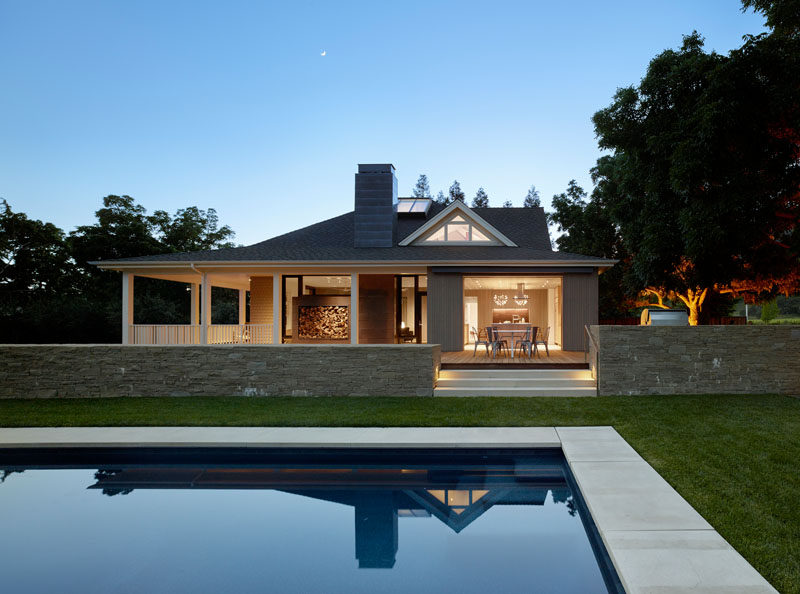 Off the side of this renovated farmhouse is a swimming pool surrounded by grass, and the porch extended out to a deck with an outdoor dining table and bbq area.