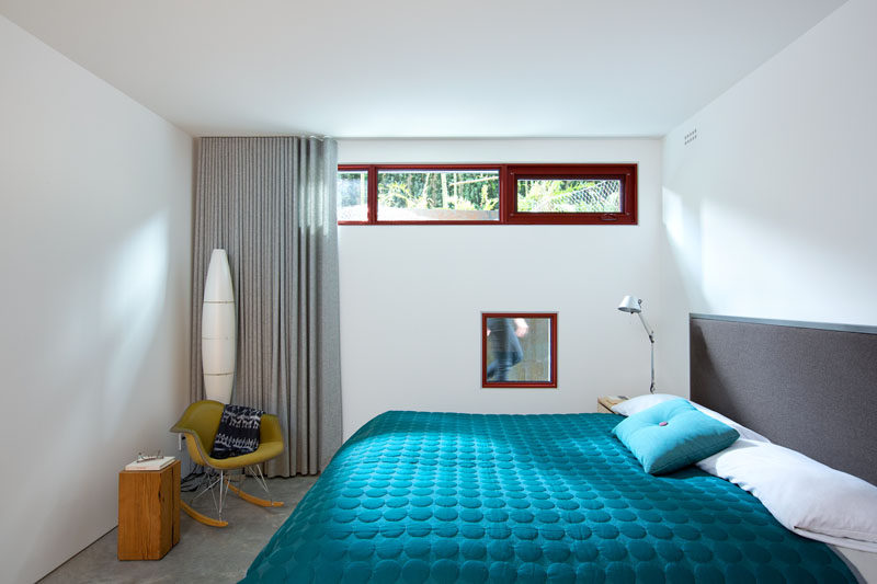 This modern bedroom has bright white walls, multiple small windows and a bright blue blanket on the bed for a pop of color.