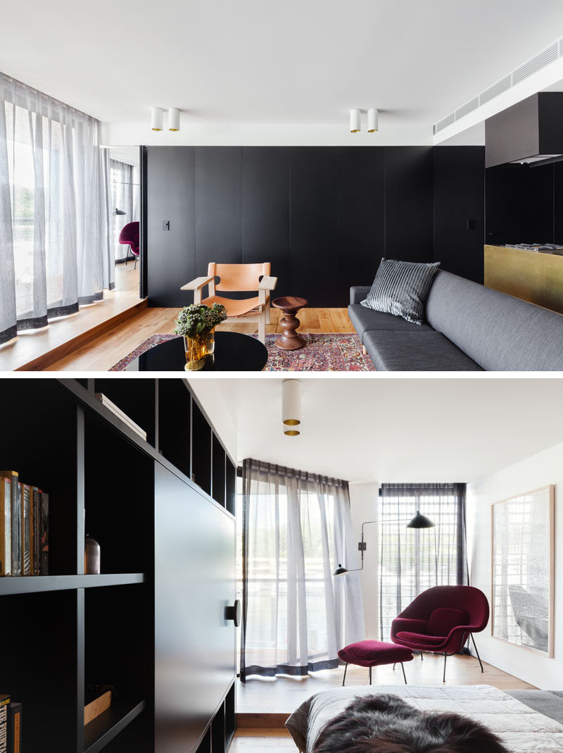 Hidden within a wall of black cabinets in this apartment is a door that leads to the bedroom. Inside the bedroom, there's a raised platform with a comfortable chair for relaxing and watching the boats outside.