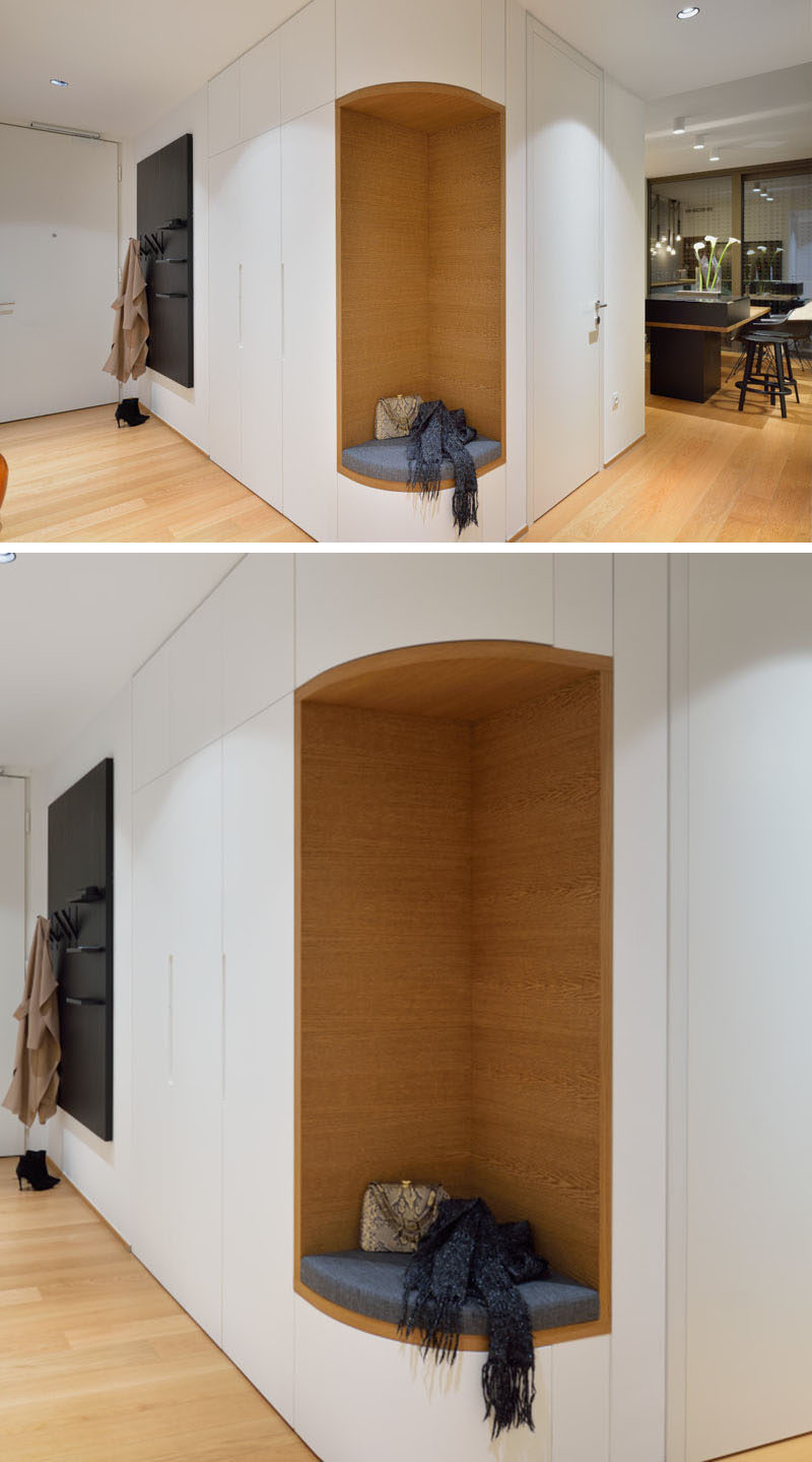 This entryway in a modern apartment has a small section of cabinets, however instead of the cabinets wrapping around the corner, the designers removed a section included a small seat with a cushion surrounded by wood, making it the ideal place to put your shoes on.