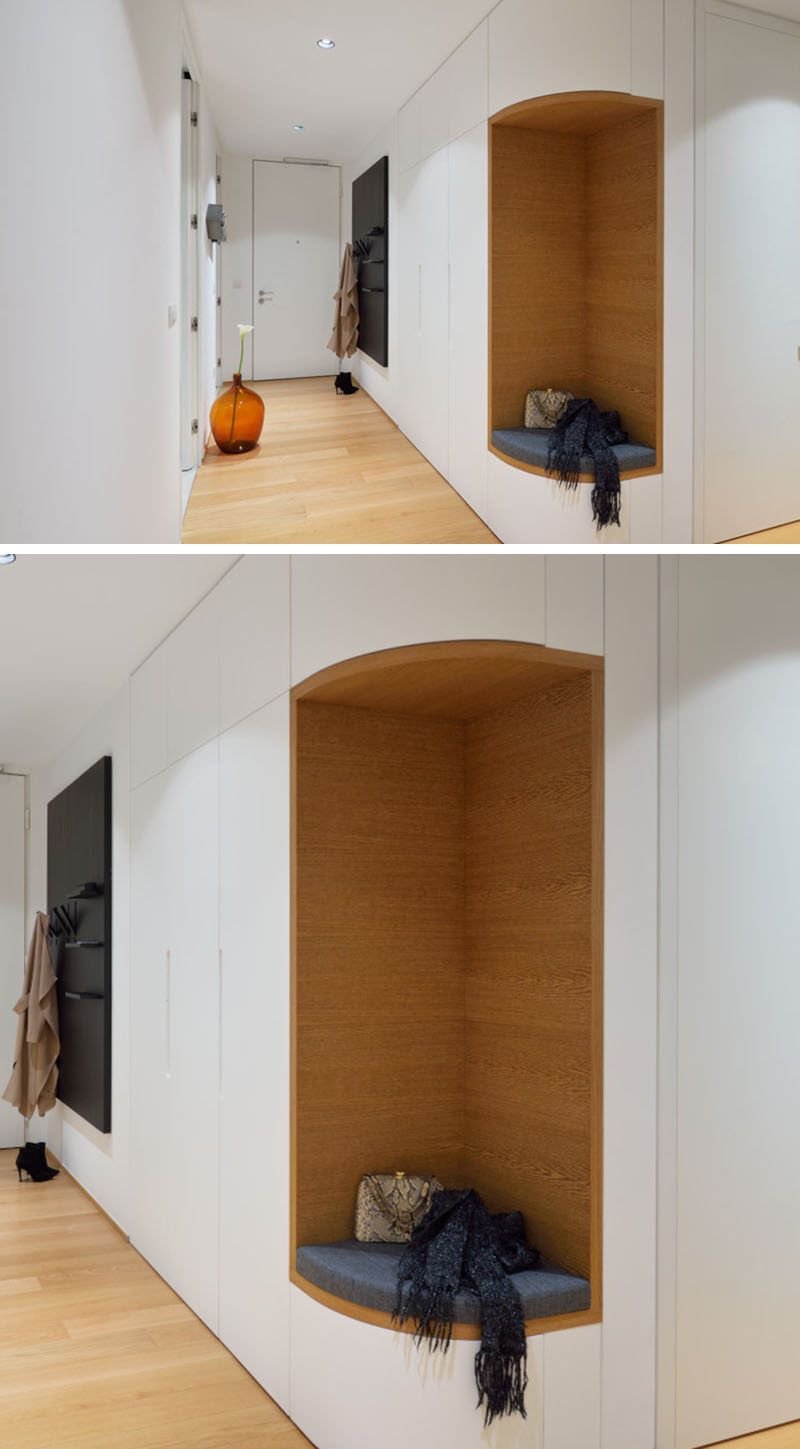 This entryway in a modern apartment has a small section of cabinets, however instead of the cabinets wrapping around the corner, the designers removed a section included a small seat with a cushion surrounded by wood, making it the ideal place to put your shoes on.