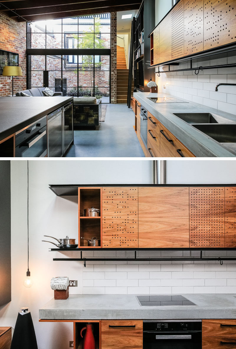 This industrial modern kitchen features a concrete countertop, wood cabinets and black hardware. Small holes have been used to create an artistic pattern on the light wood upper kitchen cabinets.