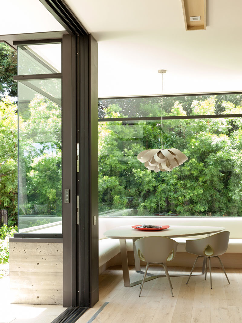 This modern house has a built-in corner breakfast nook right next to the kitchen. Large windows wrap around the corner and flood the space with natural light.