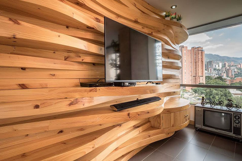 This modern apartment features a wavy wood accent wall that adds warmth to the interior, and also doubles as shelving for the television and decorative home decor items.