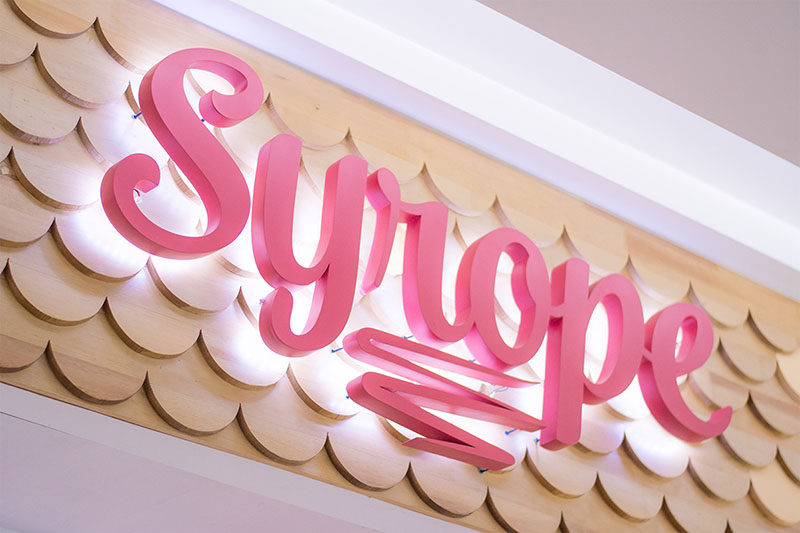 This modern retail store logo stands out from the scalloped wood facade by being slightly raised, while hidden lighting helps to highlight the business name.