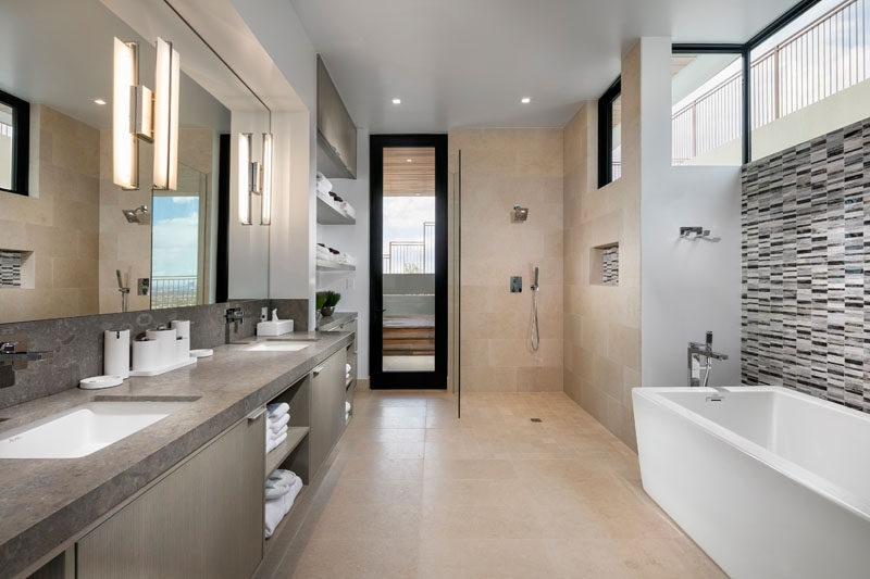 This modern master bathroom has a large vanity with dual sinks, plenty of storage space in the added cabinetry opposite the walk-in shower with a glass surround, and a standalone bathtub with patterned tile accent wall.