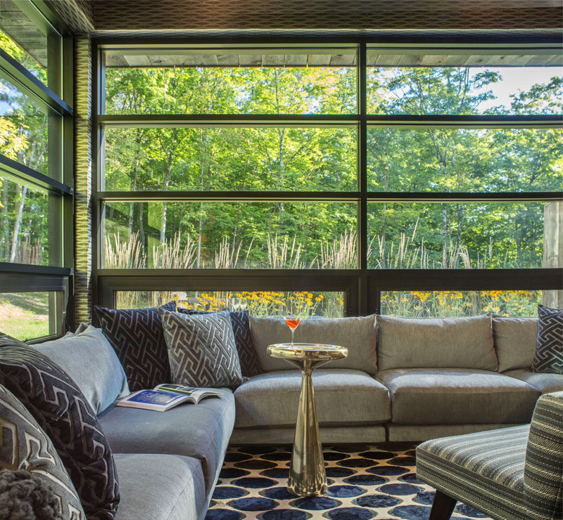 This contemporary living room has a corner sofa that wraps around the space, and black framed windows let plenty of natural light into the room and provide views of the landscape outside.