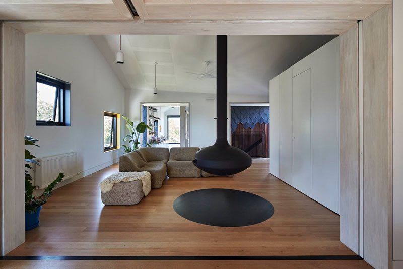 This modern living room with a wooden floor features a hanging black fireplace that matches the black window frames.