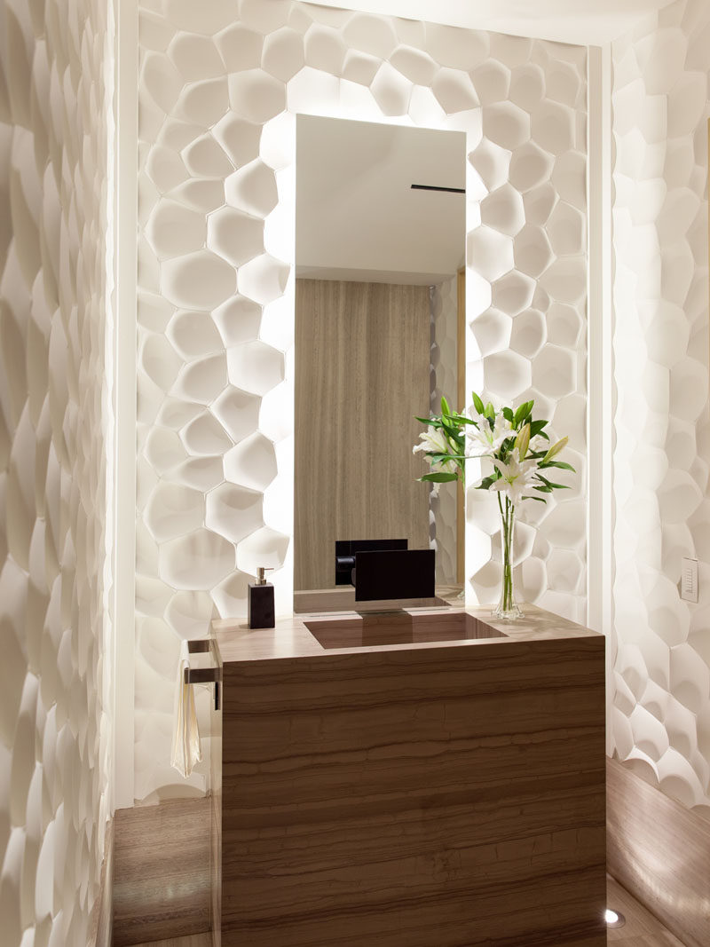 In this small and modern bathroom, sculptural white panels surround a backlit mirror.