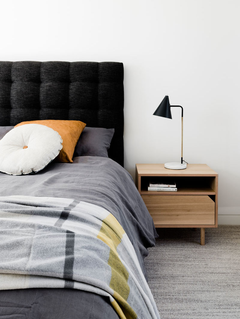 In this modern bedroom, the walls and flooring have been kept light. The dark grey upholstered headboard and the black lamp create contrast, and the light wood nightstand ties in with the other wood elements in the home.