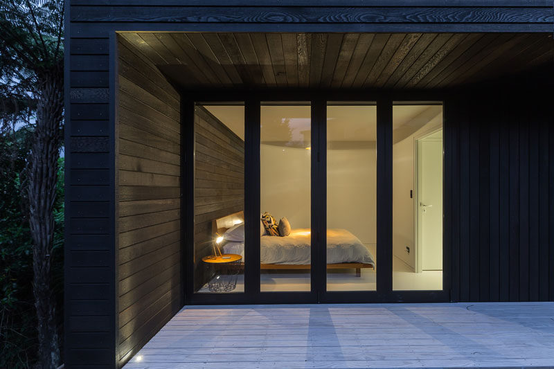 The black wood exterior siding on this small modern house continues through to act as a feature wall in this bedroom.