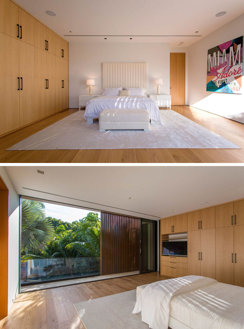 This modern bedroom has a wall full of wood cabinetry with contrasting black hardware, and it also opens up to a balcony.