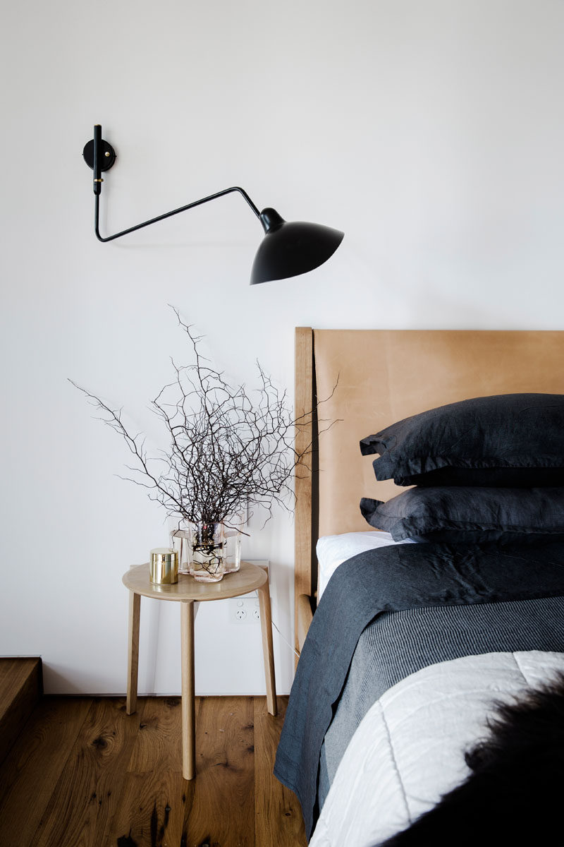 This modern bedroom features a black wall lamp, and a wood bed frame with a leather headboard.