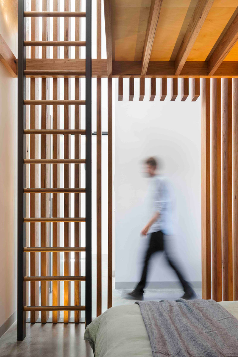 This modern bedroom has a wall of wood slats and a ladder that leads to a loft.