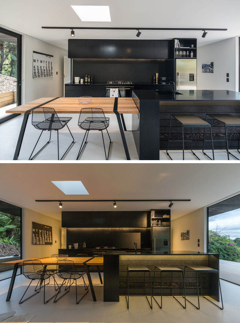This modern black kitchen has a large island with a wood dining table at one end. Black accents like the chairs, table details and track lighting have also been included.
