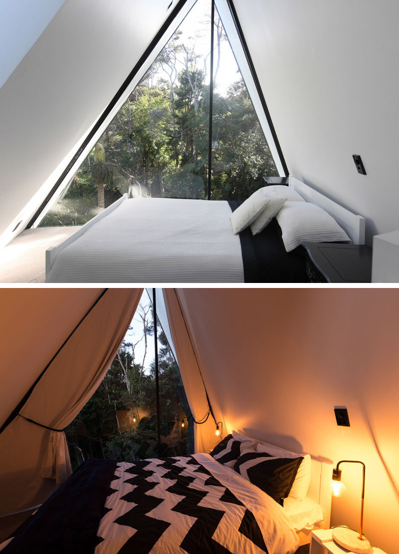 The bedroom in this modern cabin has a view of the treetops, and also has draped curtains, much like the entryway to a tent.