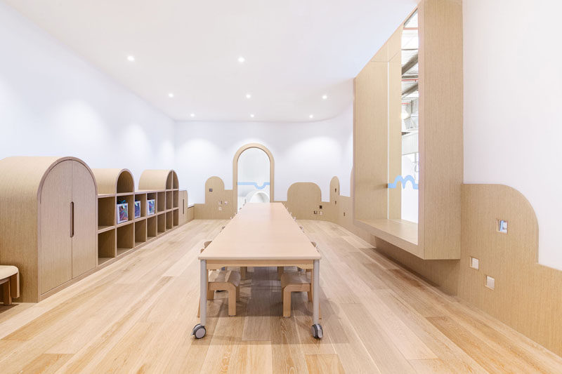 In this modern playroom, there's a single long table on wheels for groups of children, and curved wood details along the walls spark the children's imagination and allow them to believe they could be buildings, mountains, or anything else their minds think of.