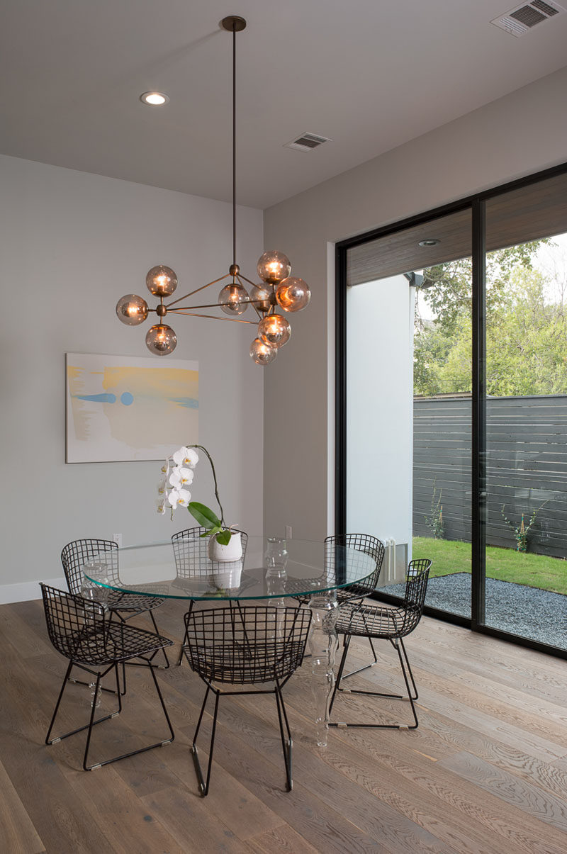 A sculptural glass pendant light anchors the round glass dining table in the open floor plan. Large windows provide views of the garden outside.