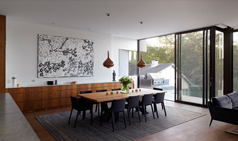 In this modern house, the dining room is located just off the kitchen, and the wood kitchen cabinets continue through to become a long sideboard. 