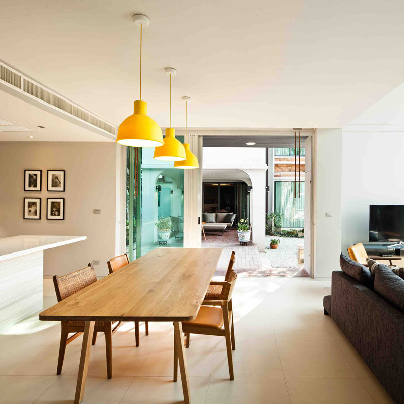 This modern dining room is made up of a large wood dining table with three yellow pendant lights adding a pop of colour to the space. 