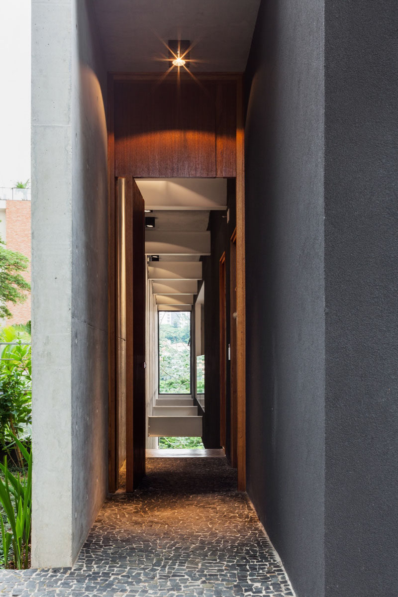 At the front of this modern house, a tall wood front door lit by a single light, sits beside the garage.