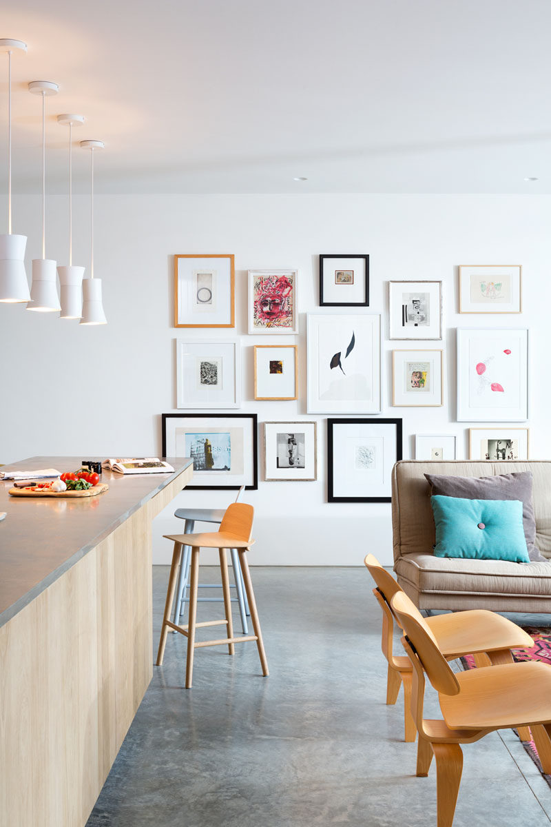 Between the living room and the kitchen in this modern house, is a wall decorated with a gallery of favorite art pieces.