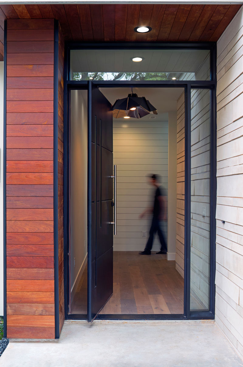 Welcoming you to this modern house is a large matte black pivoting front door, that's surrounded by windows, letting the natural light shine into the the home.